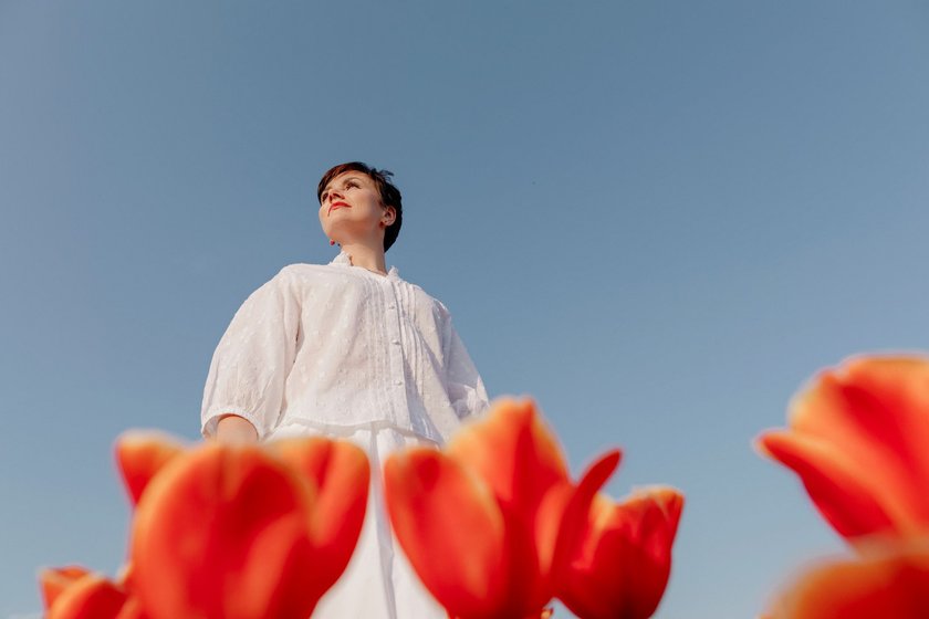 Eine Frau steht vor einem blauen Himmel und vor ihr wachsen schöne Tulpen